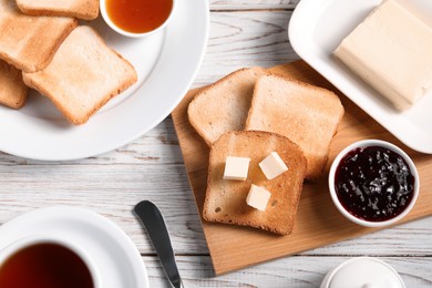 Photo of Slices of tasty toasted bread with butter and jam on light wooden table, flat lay