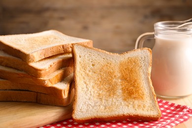 Photo of Slices of tasty toasted bread and jug of milk on wooden table, closeup