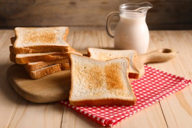 Photo of Slices of tasty toasted bread and jug of milk on wooden table, closeup