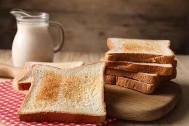 Photo of Slices of tasty toasted bread and jug of milk on wooden table, closeup
