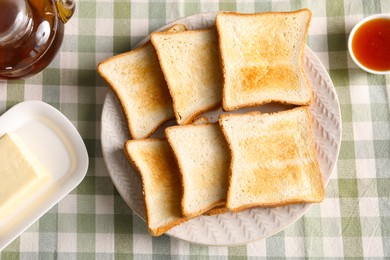 Photo of Slices of tasty toasted bread, butter and jam on checkered tablecloth, flat lay