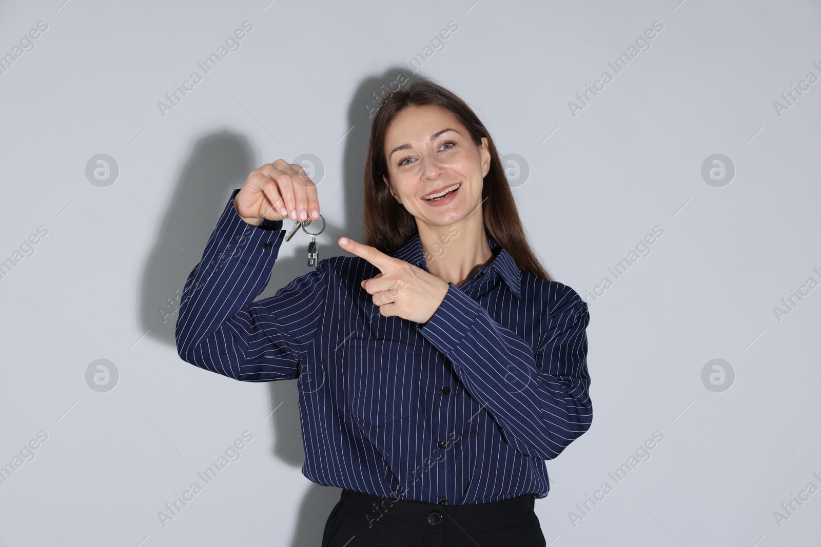 Real estate agent holding key with house shaped keychain on light grey background Photo of Real estate agent holding key with house shaped keychain on light grey background