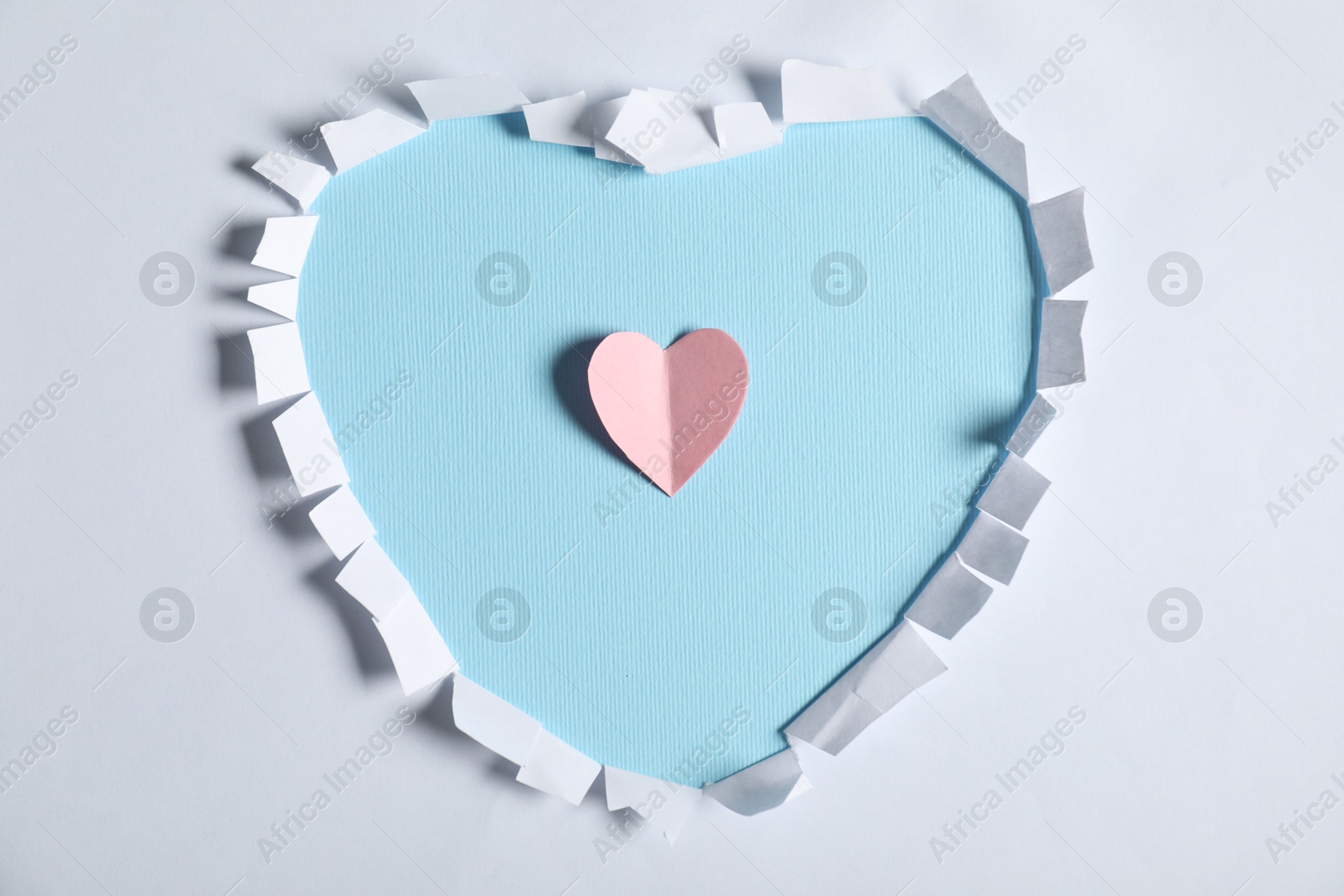 White paper with hole in shape of heart and pink one on light blue background, top view Photo of White paper with hole in shape of heart and pink one on light blue background, top view