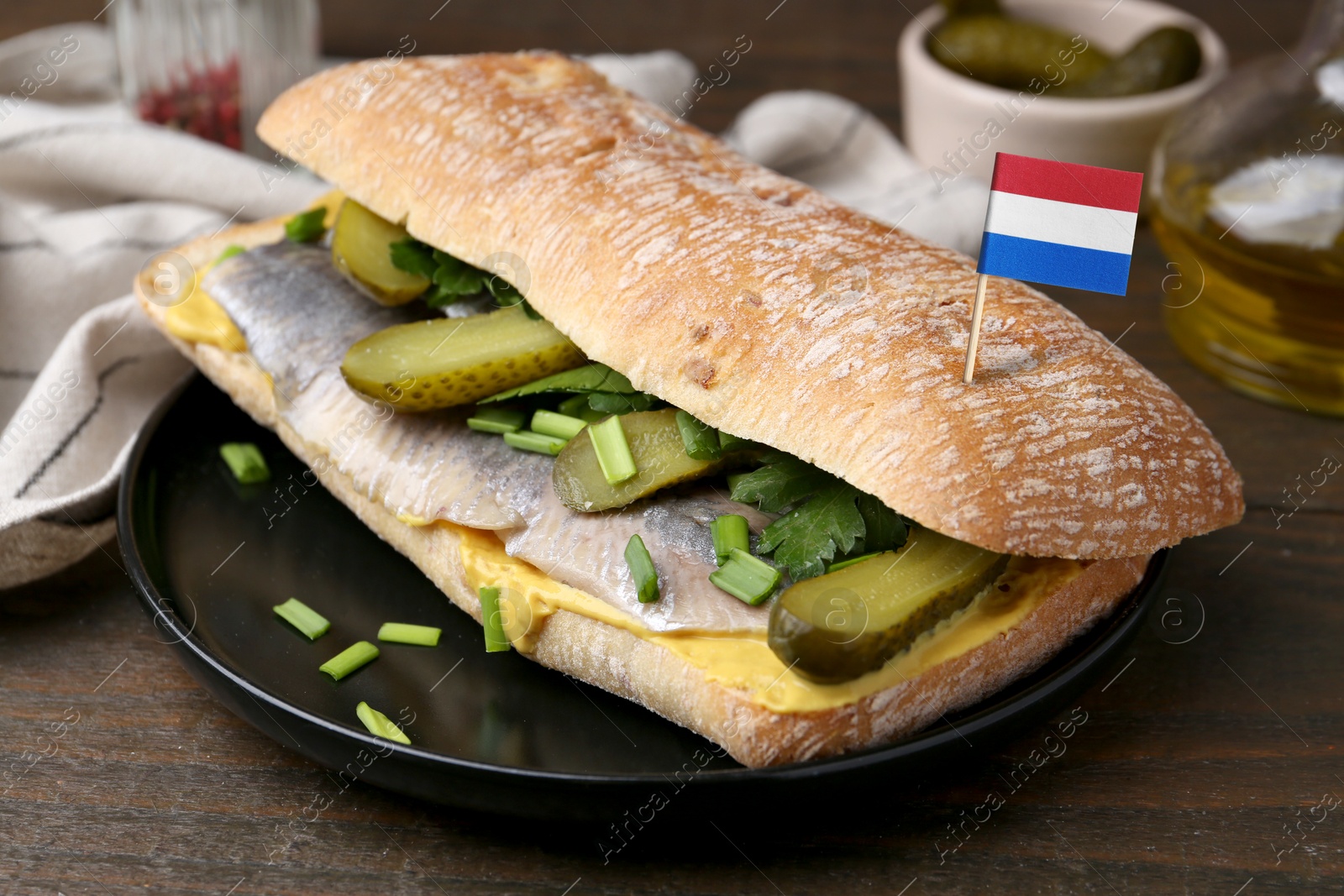 Tasty sandwich with herring, pickles and flag of Netherlands on wooden table, closeup Image of Tasty sandwich with herring, pickles and flag of Netherlands on wooden table, closeup