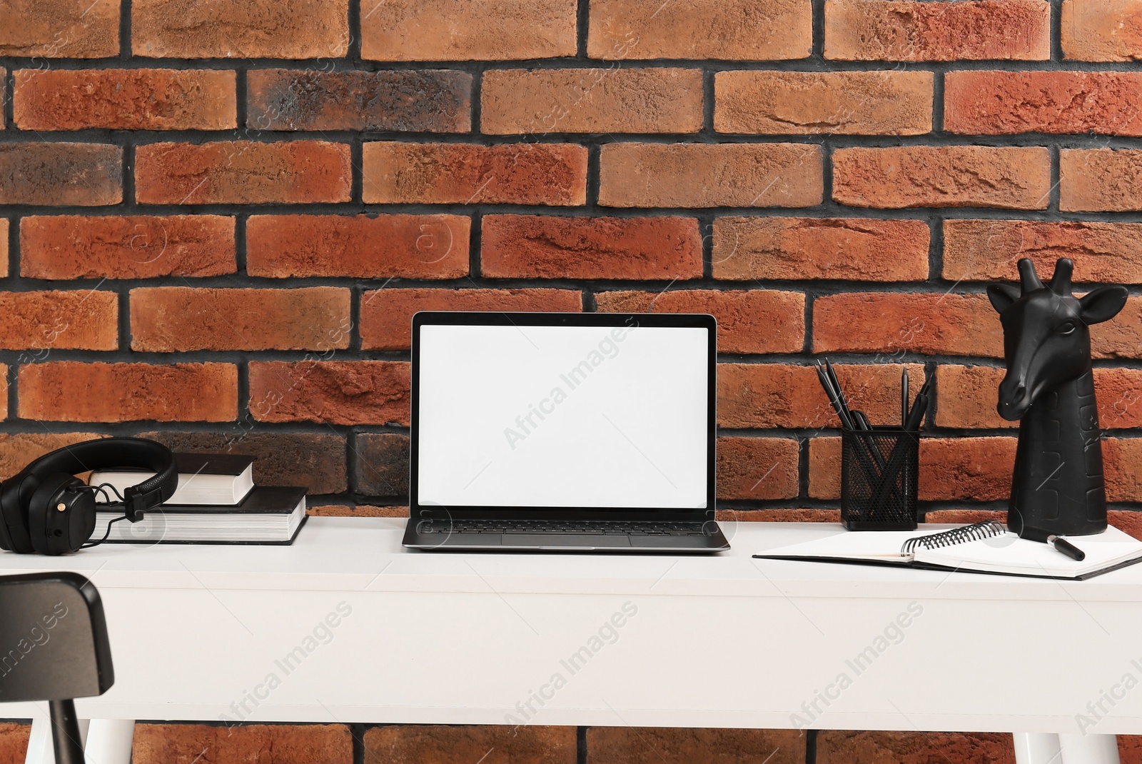 Stylish workplace with laptop, headphones, stationary and decor on white table near brick wall Photo of Stylish workplace with laptop, headphones, stationary and decor on white table near brick wall