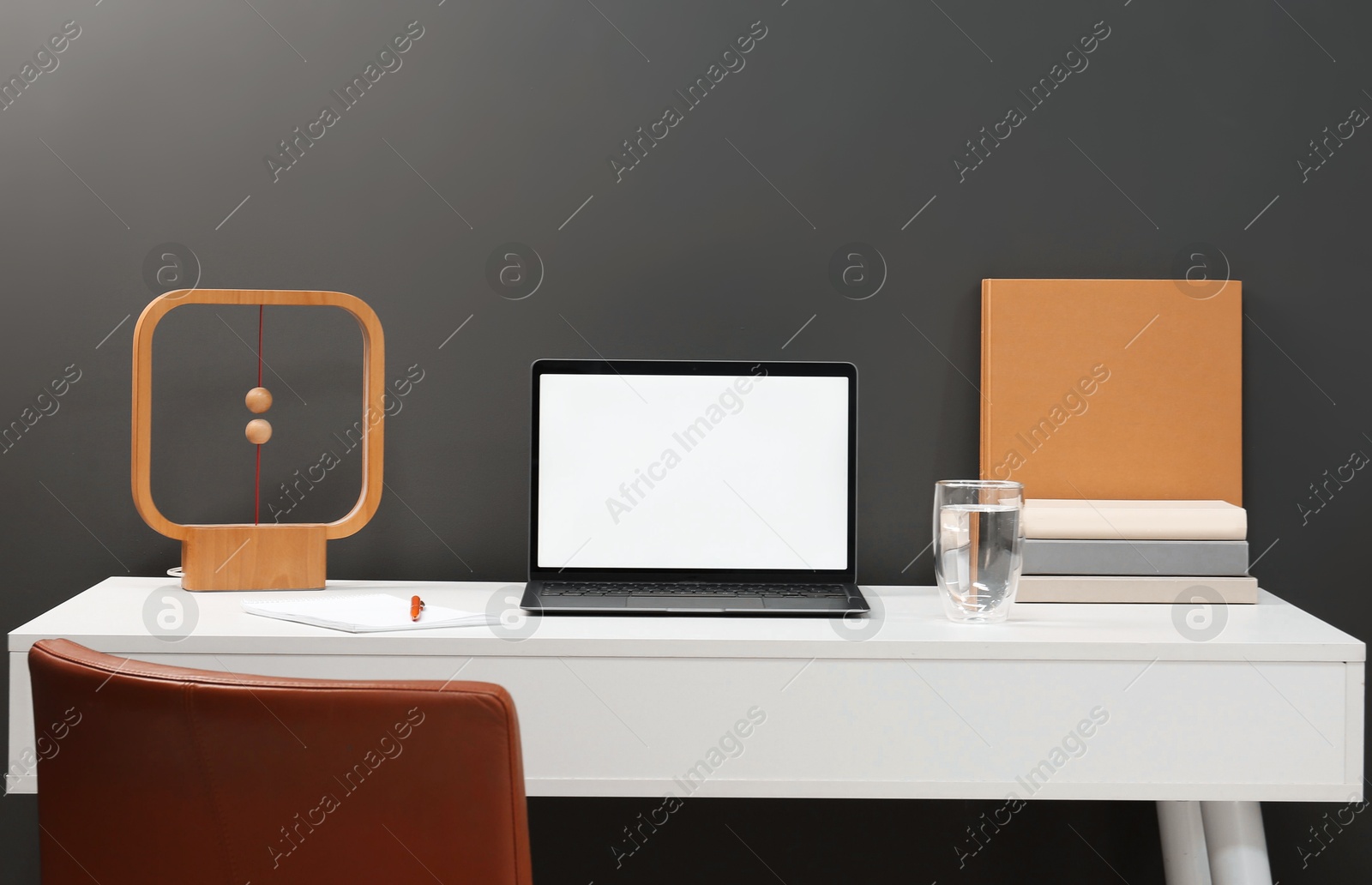 Stylish workplace with laptop, glass of water, books and decor on white table near grey wall Photo of Stylish workplace with laptop, glass of water, books and decor on white table near grey wall