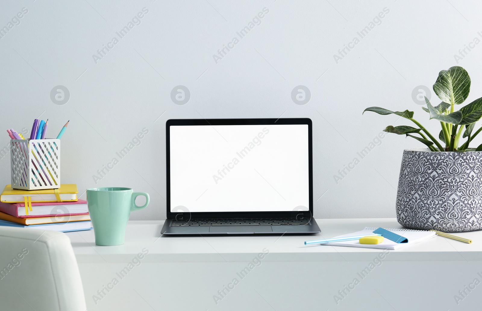 Stylish workplace with laptop, houseplant, stationary and cup on table near white wall Photo of Stylish workplace with laptop, houseplant, stationary and cup on table near white wall