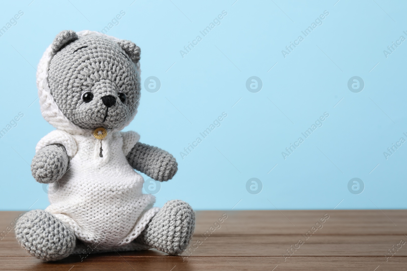 Photo of Cute knitted toy bear on wooden table against light blue background. Space for text