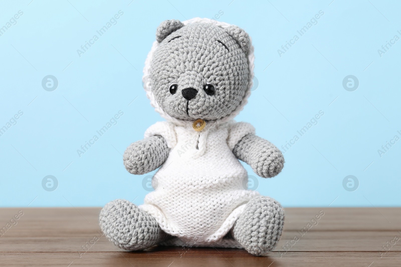 Cute knitted toy bear on wooden table against light blue background Photo of Cute knitted toy bear on wooden table against light blue background