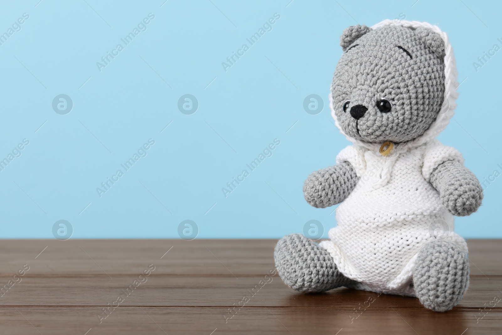 Photo of Cute knitted toy bear on wooden table against light blue background. Space for text