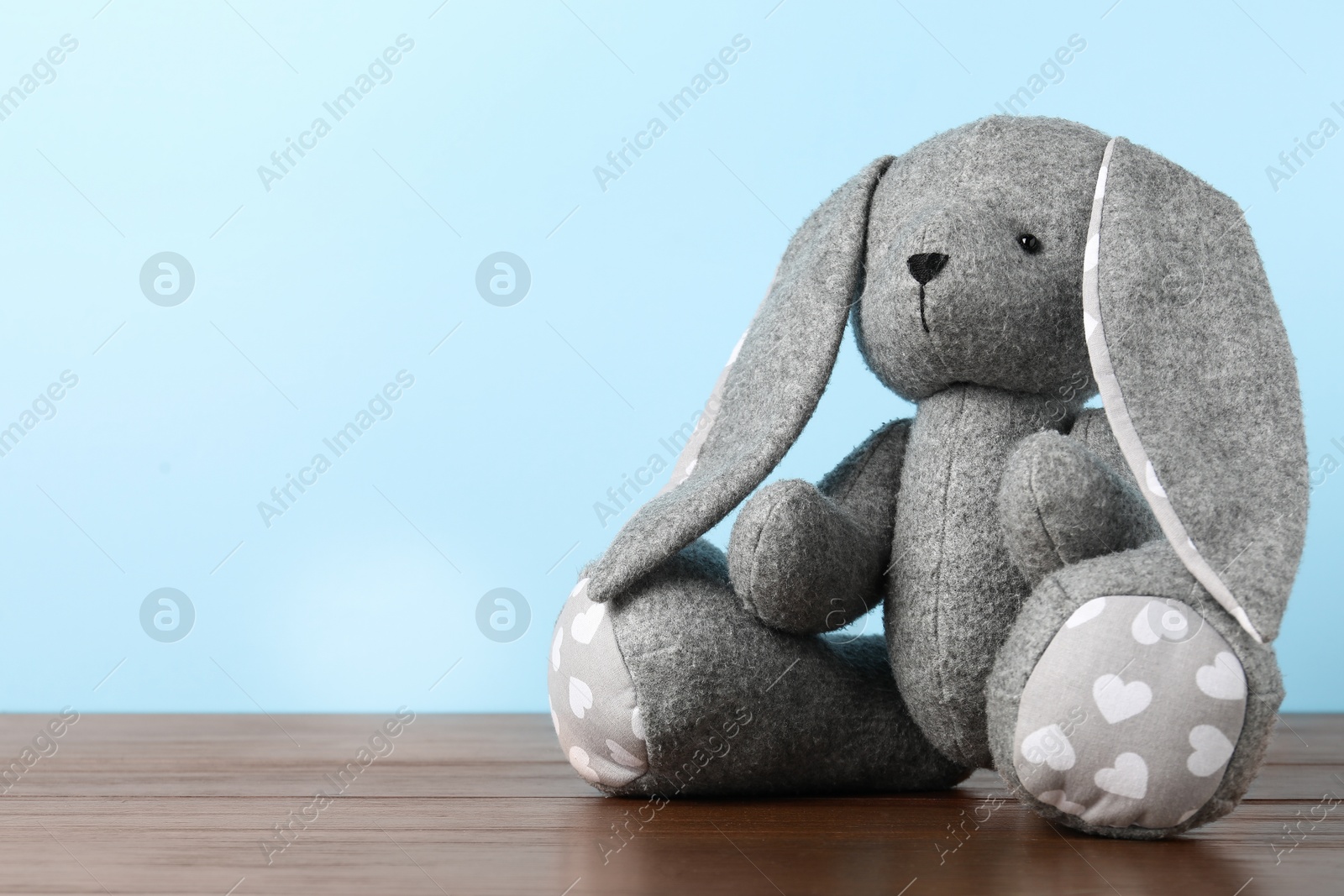 Photo of Cute toy bunny on wooden table against light blue background. Space for text