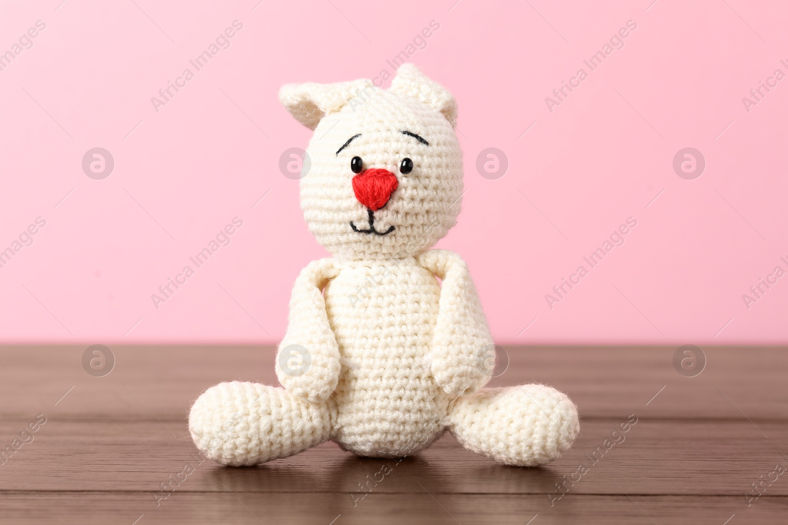 Cute knitted toy bunny on wooden table against pink background Photo of Cute knitted toy bunny on wooden table against pink background