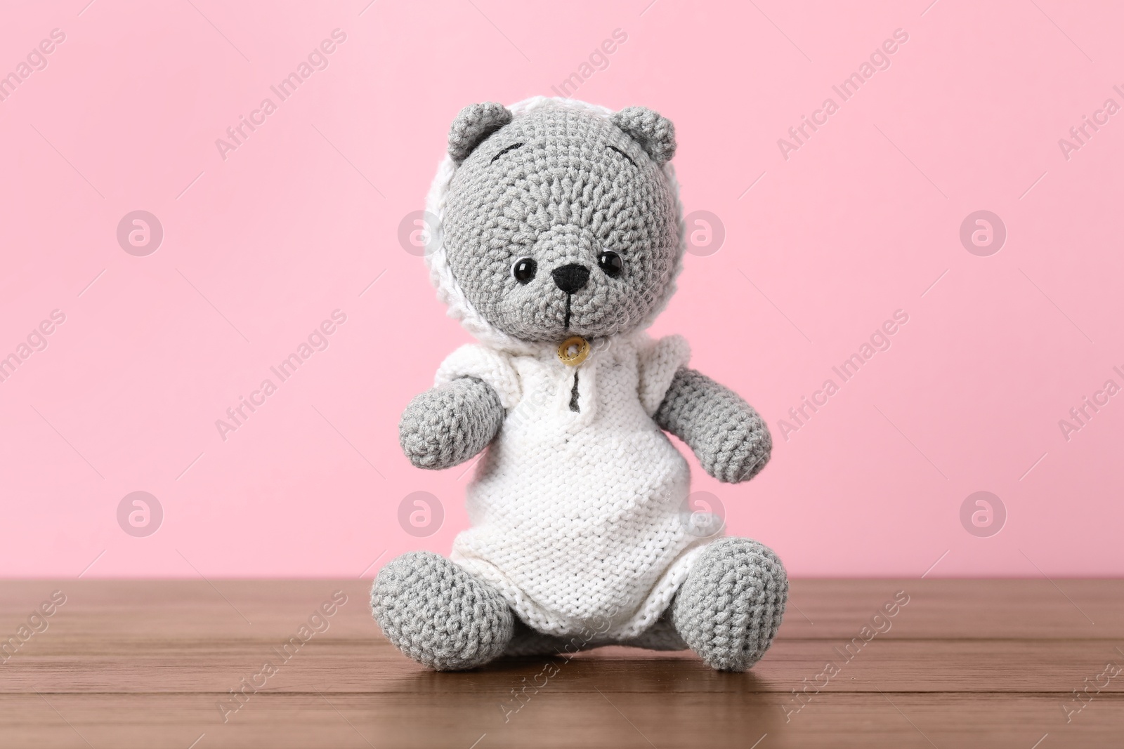 Cute knitted toy bear on wooden table against pink background Photo of Cute knitted toy bear on wooden table against pink background