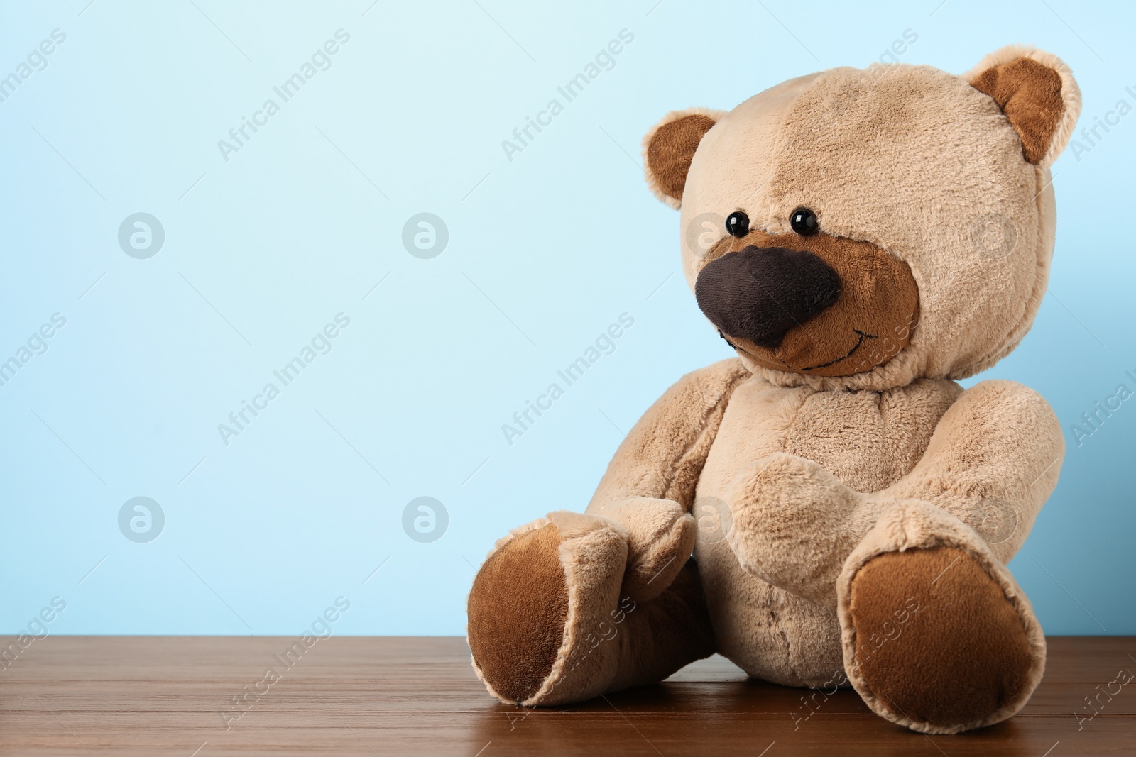Cute teddy bear on wooden table against light blue background. Space for text Photo of Cute teddy bear on wooden table against light blue background. Space for text