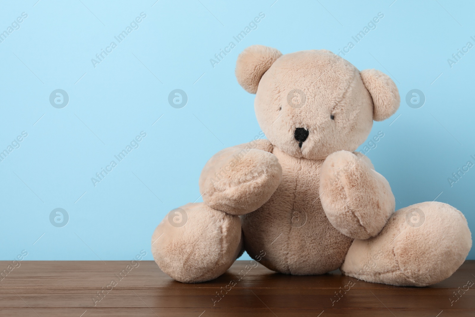 Photo of Cute teddy bear on wooden table against light blue background. Space for text