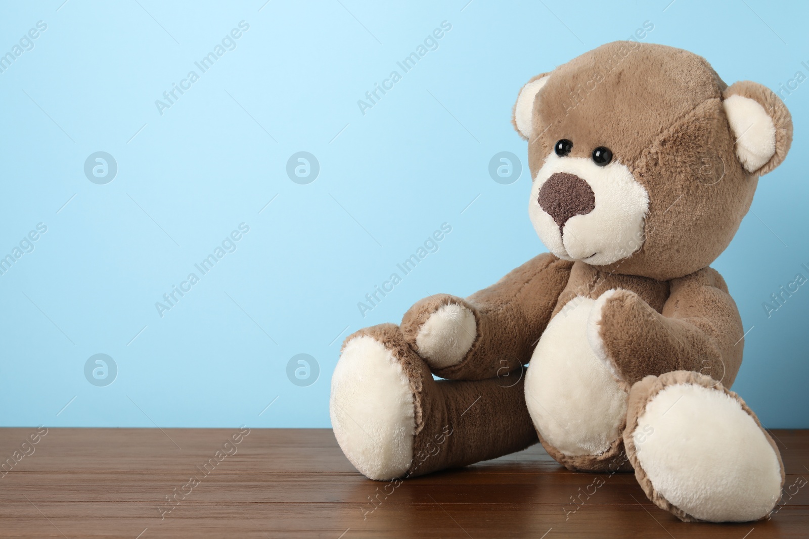 Cute teddy bear on wooden table against light blue background. Space for text Photo of Cute teddy bear on wooden table against light blue background. Space for text