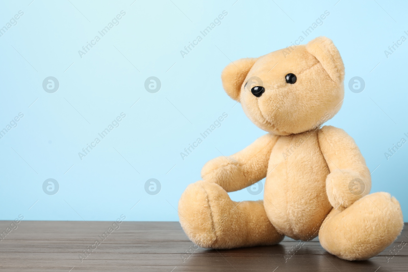 Cute teddy bear on wooden table against light blue background. Space for text Photo of Cute teddy bear on wooden table against light blue background. Space for text