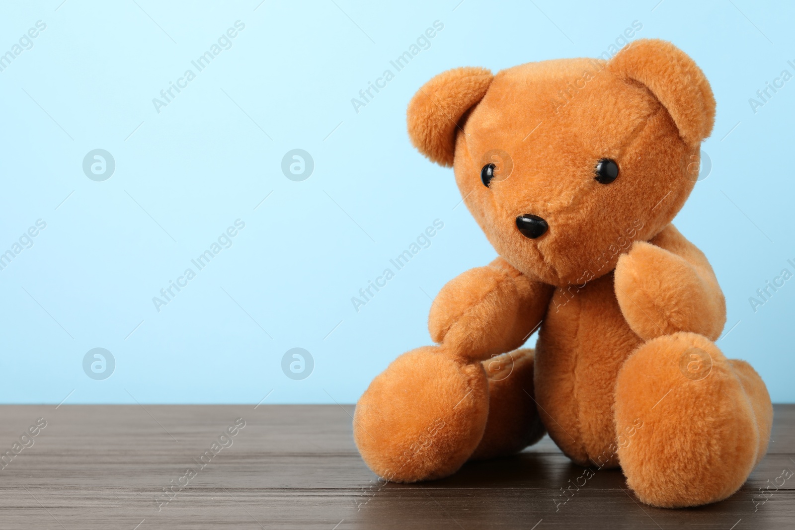 Cute teddy bear on wooden table against light blue background. Space for text Photo of Cute teddy bear on wooden table against light blue background. Space for text