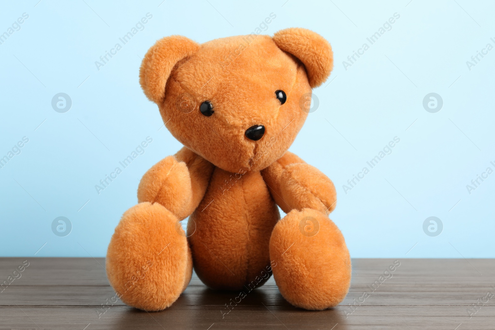 Photo of Cute teddy bear on wooden table against light blue background
