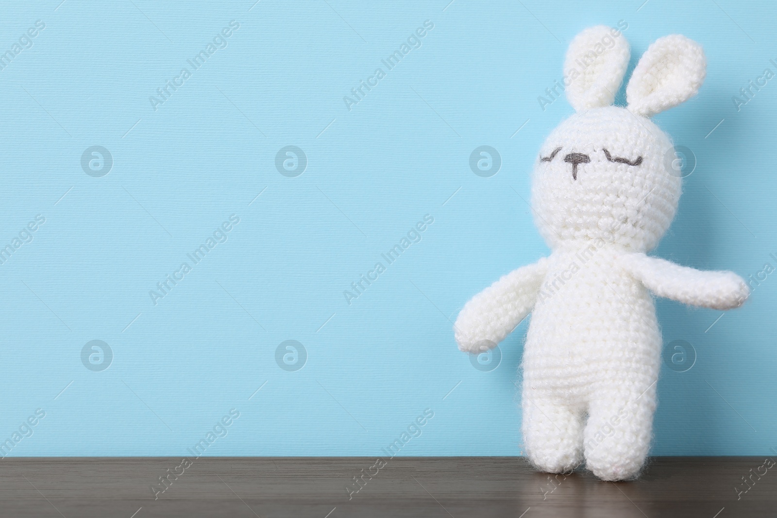 Cute knitted toy bunny on wooden table against light blue background. Space for text Photo of Cute knitted toy bunny on wooden table against light blue background. Space for text
