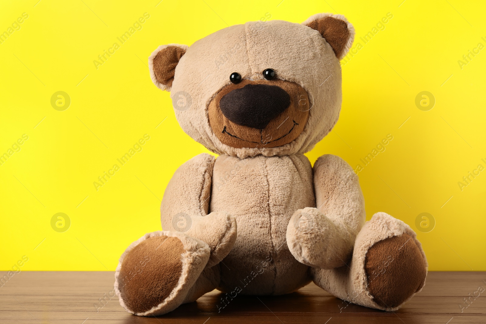 Cute teddy bear on wooden table against yellow background Photo of Cute teddy bear on wooden table against yellow background