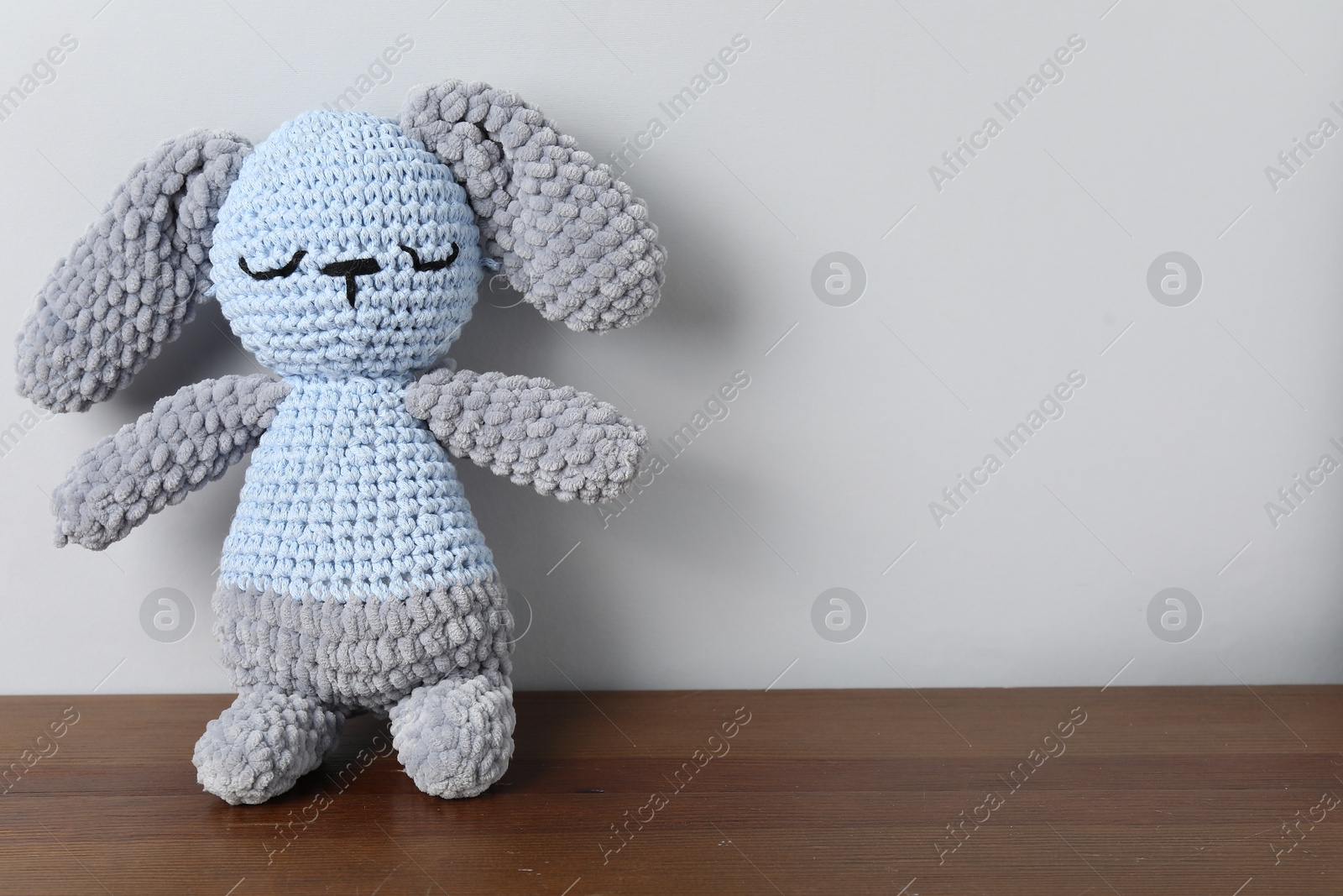 Cute knitted toy bunny on wooden table against light background. Space for text Photo of Cute knitted toy bunny on wooden table against light background. Space for text