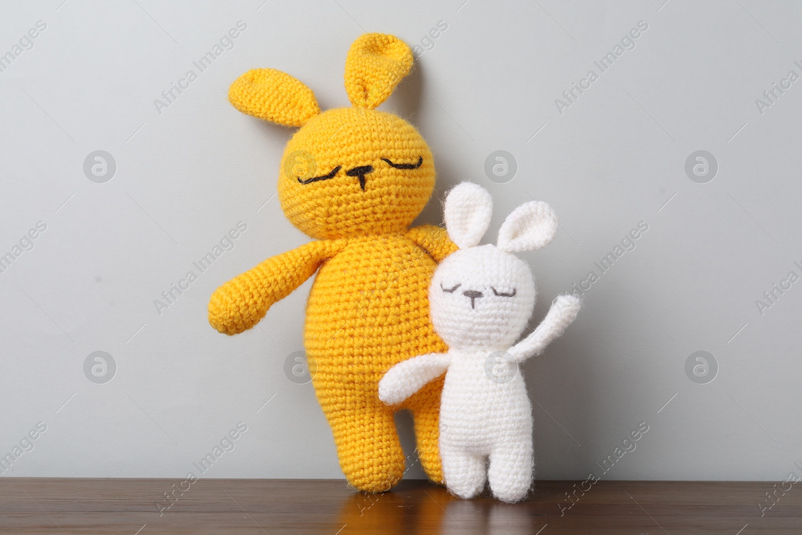 Cute knitted toy bunnies on wooden table against light background Photo of Cute knitted toy bunnies on wooden table against light background