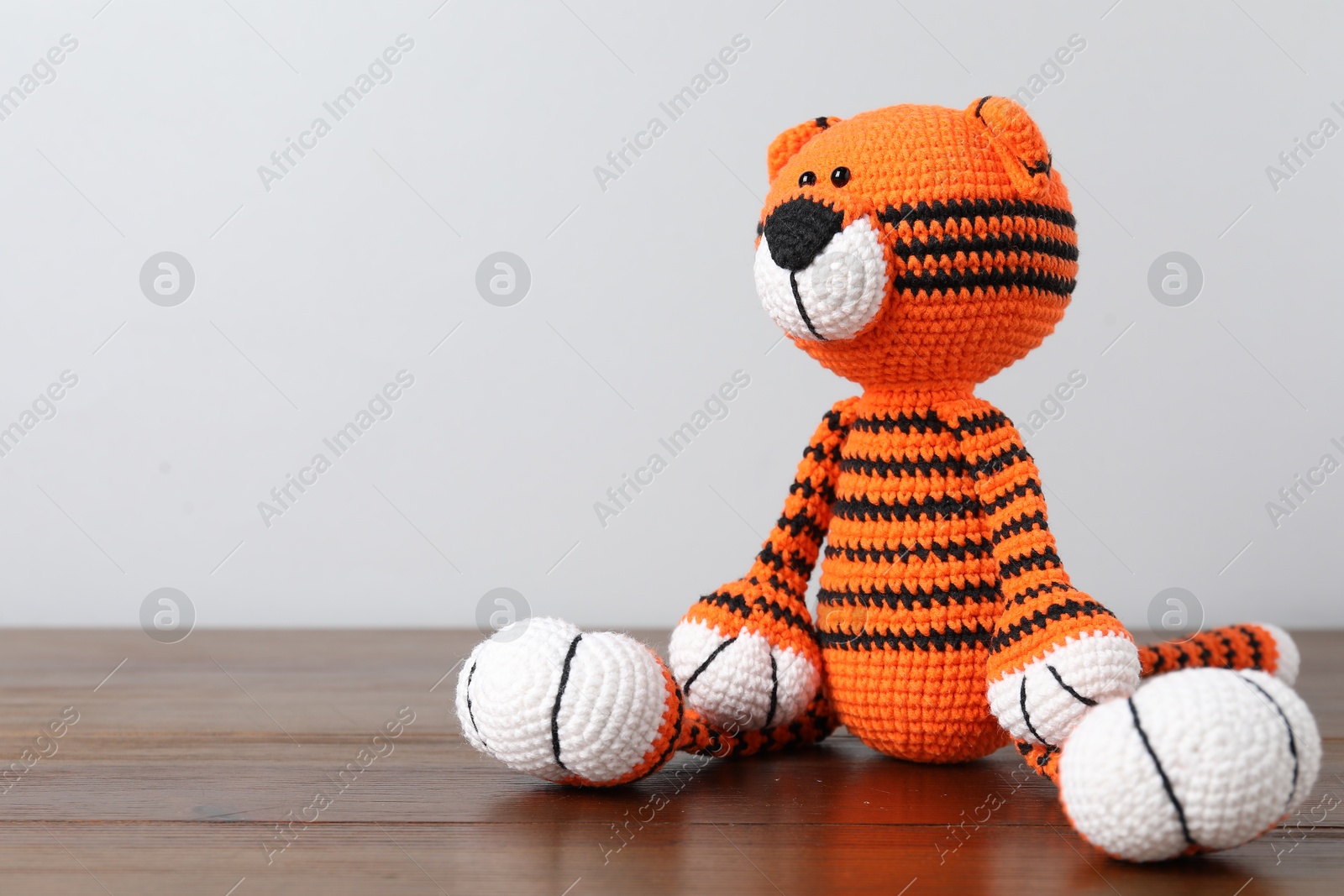 Cute knitted toy tiger on wooden table against light background. Space for text Photo of Cute knitted toy tiger on wooden table against light background. Space for text