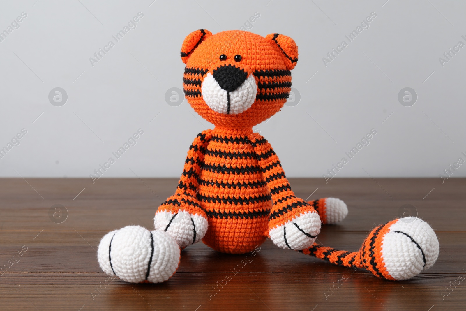 Cute knitted toy tiger on wooden table against light background Photo of Cute knitted toy tiger on wooden table against light background