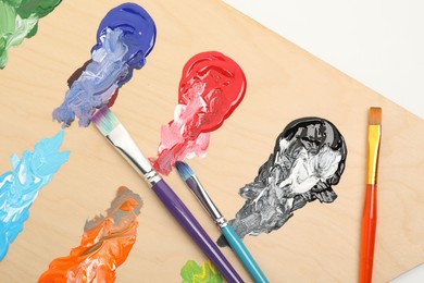 Photo of Wooden palette with paints and brushes on white background, top view