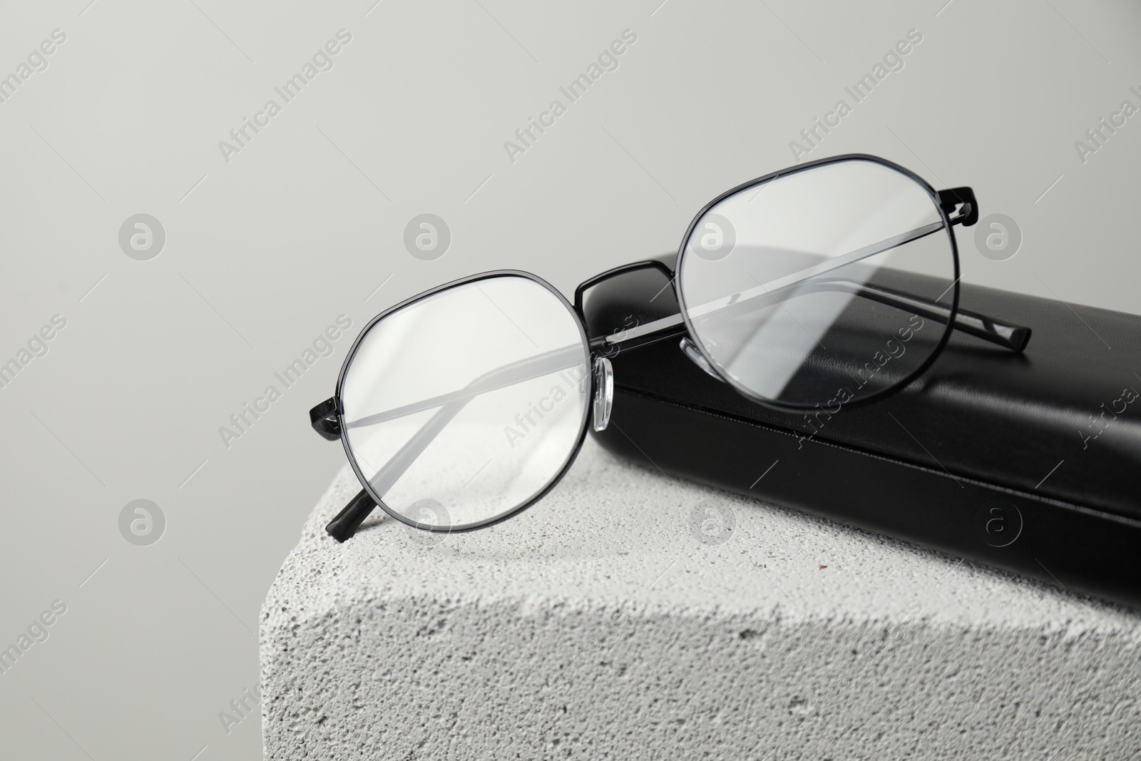 Stylish glasses and case on stone surface against light grey background, closeup. Space for text Photo of Stylish glasses and case on stone surface against light grey background, closeup. Space for text