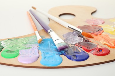 Photo of Wooden palette with paints and brushes on white background, closeup