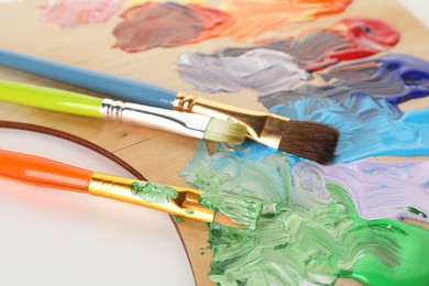 Photo of Wooden palette with paints and brushes on white background, closeup