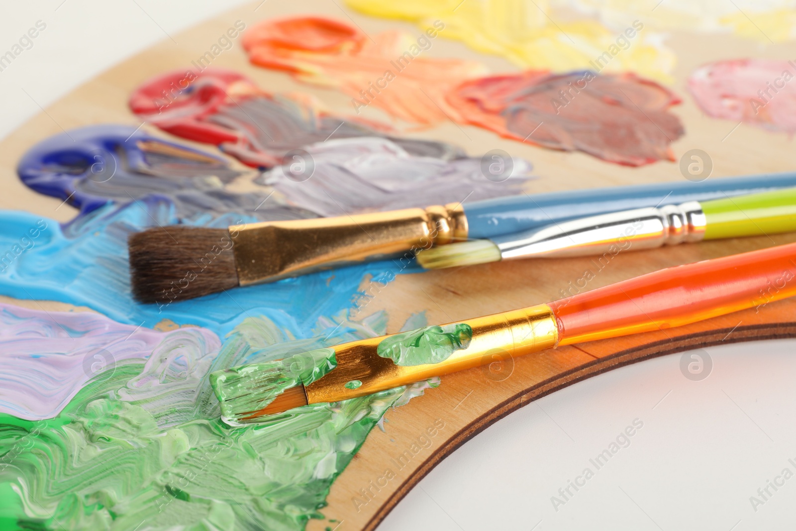 Photo of Wooden palette with paints and brushes on white background, closeup