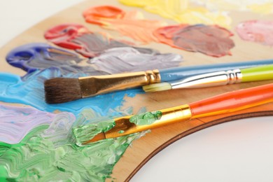 Photo of Wooden palette with paints and brushes on white background, closeup