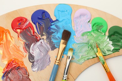 Photo of Wooden palette with paints and brushes on white background, top view