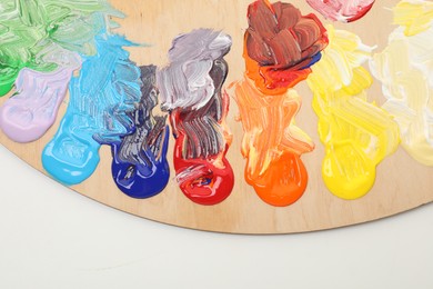 Wooden palette with paints on white background, top view
