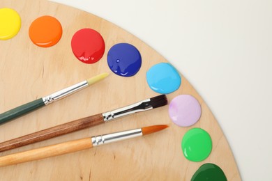 Photo of Wooden palette with paints and brushes on white background, top view