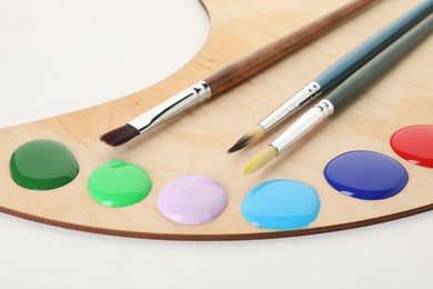 Photo of Wooden palette with paints and brushes on white background, closeup