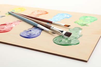 Photo of Wooden palette with paints and brushes on white background, closeup
