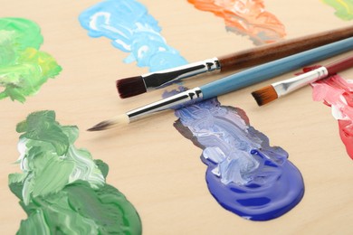 Photo of Wooden palette with paints and brushes, closeup