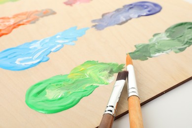 Photo of Wooden palette with paints and brushes on white background, closeup