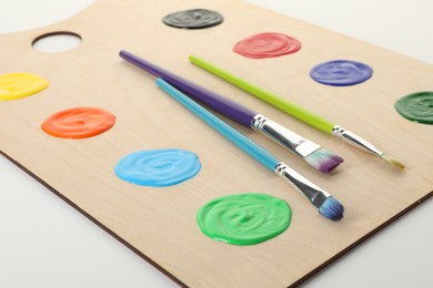 Photo of Wooden palette with paints and brushes on white background, closeup