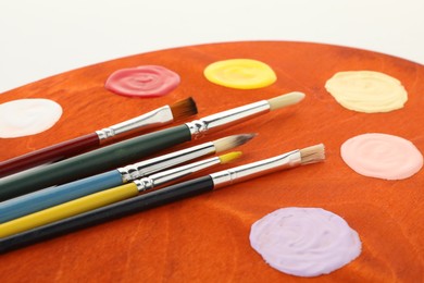 Photo of Wooden palette with paints and brushes on white background, closeup