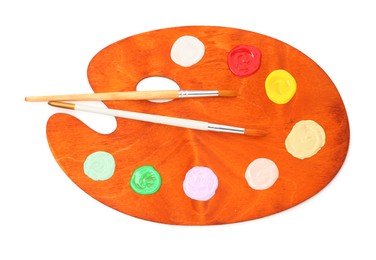 Photo of Wooden palette with paints and brushes isolated on white, top view
