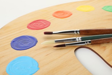 Photo of Wooden palette with paints and brushes on white background, closeup
