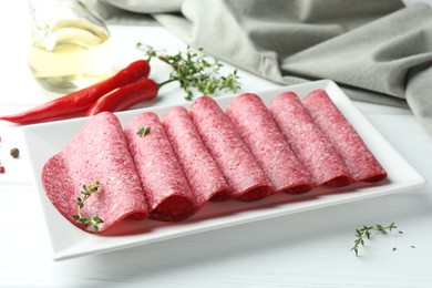 Photo of Slices of tasty smoked sausage and spices on white wooden table, closeup