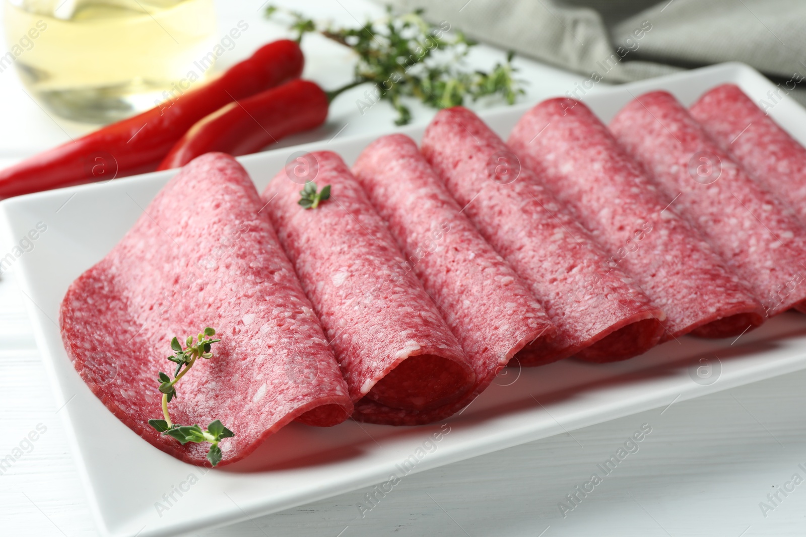 Photo of Slices of tasty smoked sausage and spices on white wooden table, closeup