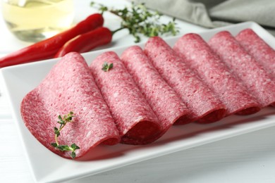 Photo of Slices of tasty smoked sausage and spices on white wooden table, closeup