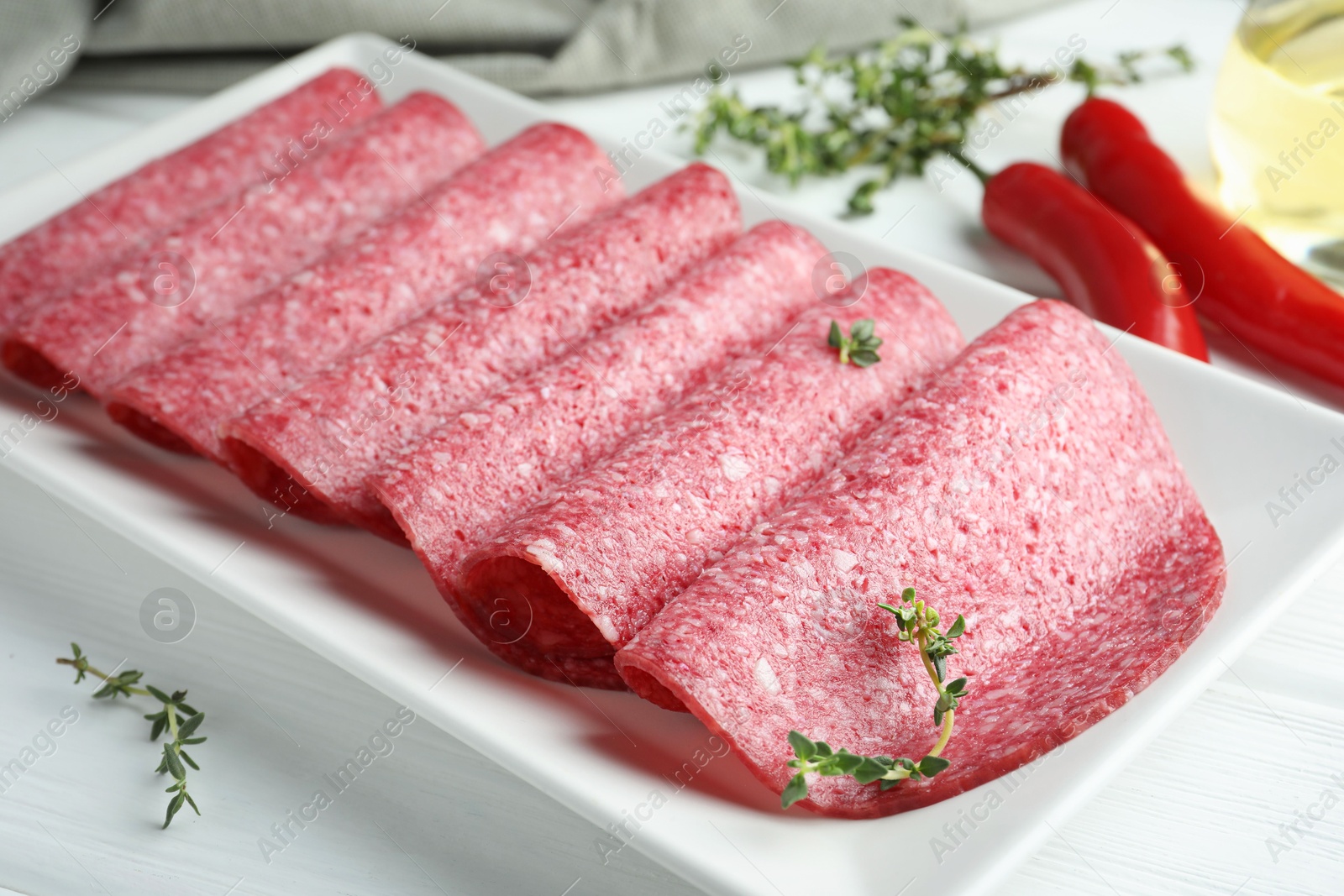 Slices of tasty smoked sausage and spices on white wooden table, closeup Photo of Slices of tasty smoked sausage and spices on white wooden table, closeup
